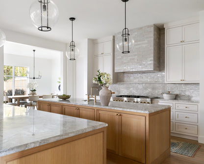 Modern kitchen with marble countertops, wooden cabinets, and off white zellige tile as backsplash.