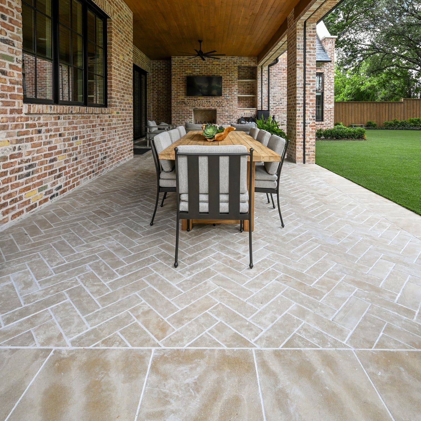 Outdoor patio with wooden table, chairs against a brick wall, and sand limestone flooring.