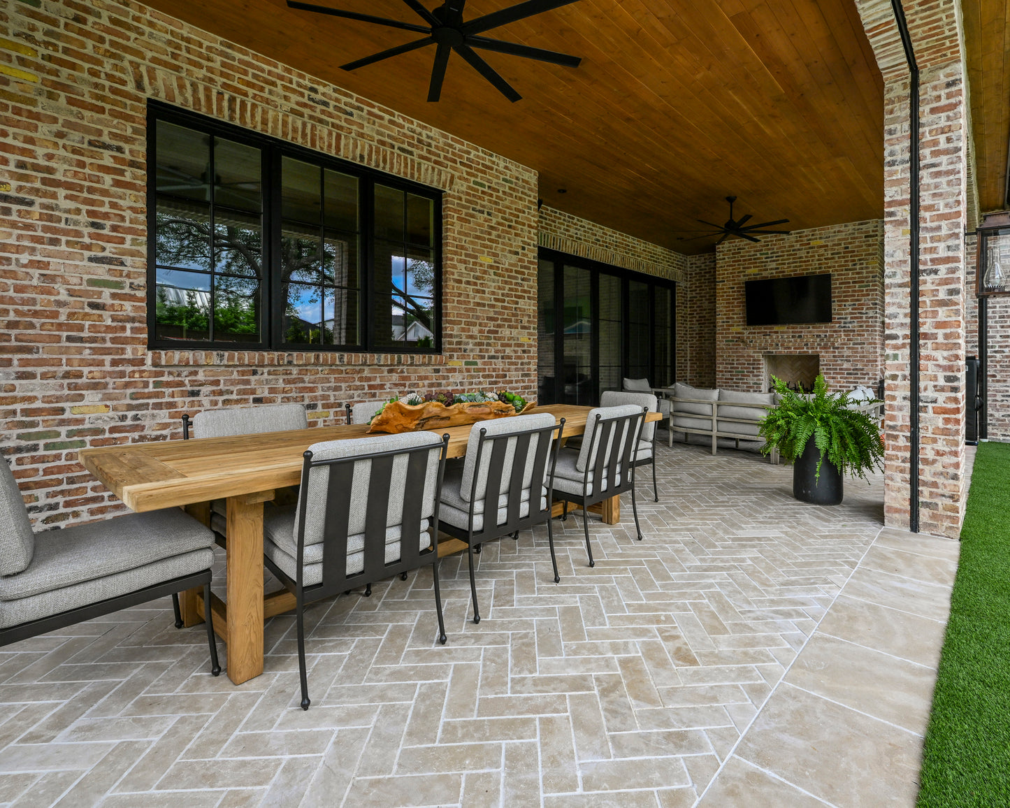 Outdoor patio with wooden table, chairs against a brick wall, and sand limestone flooring.