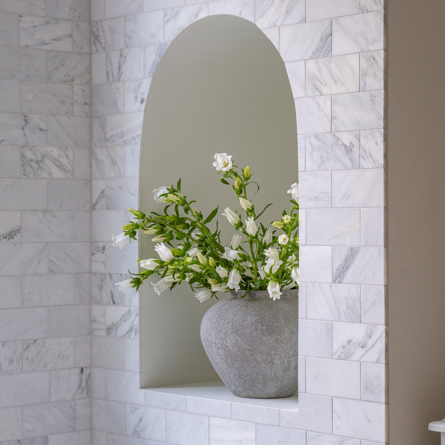 Gray vase with white flowers on a shelf against a marble wall