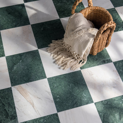 A styled floor scene with a woven basket holding a cream fringed throw blanket, placed on a green-and-white checkered marble floor.