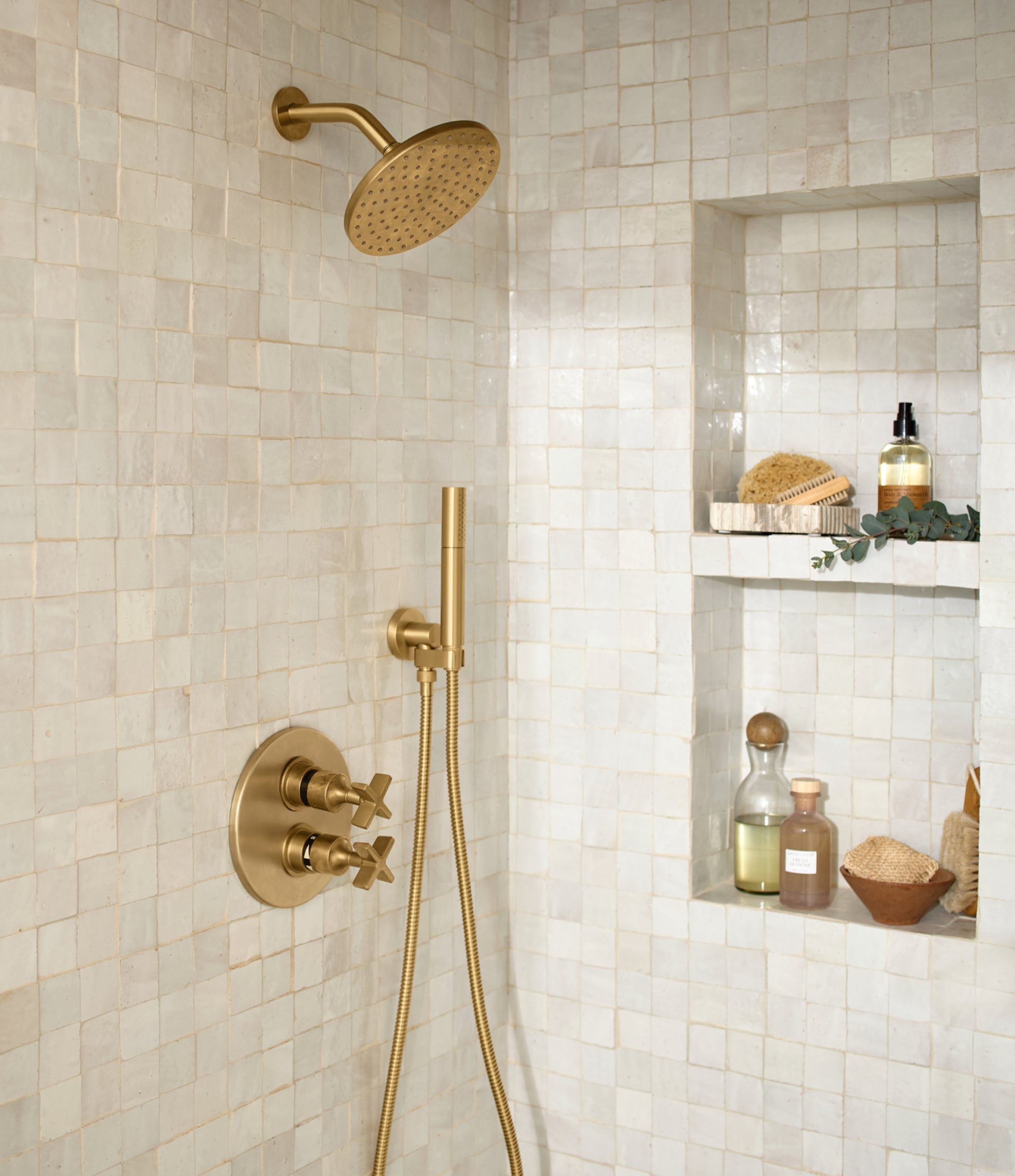 Gold shower fixture set against a tiled shower wall with a shelf holding bath products.