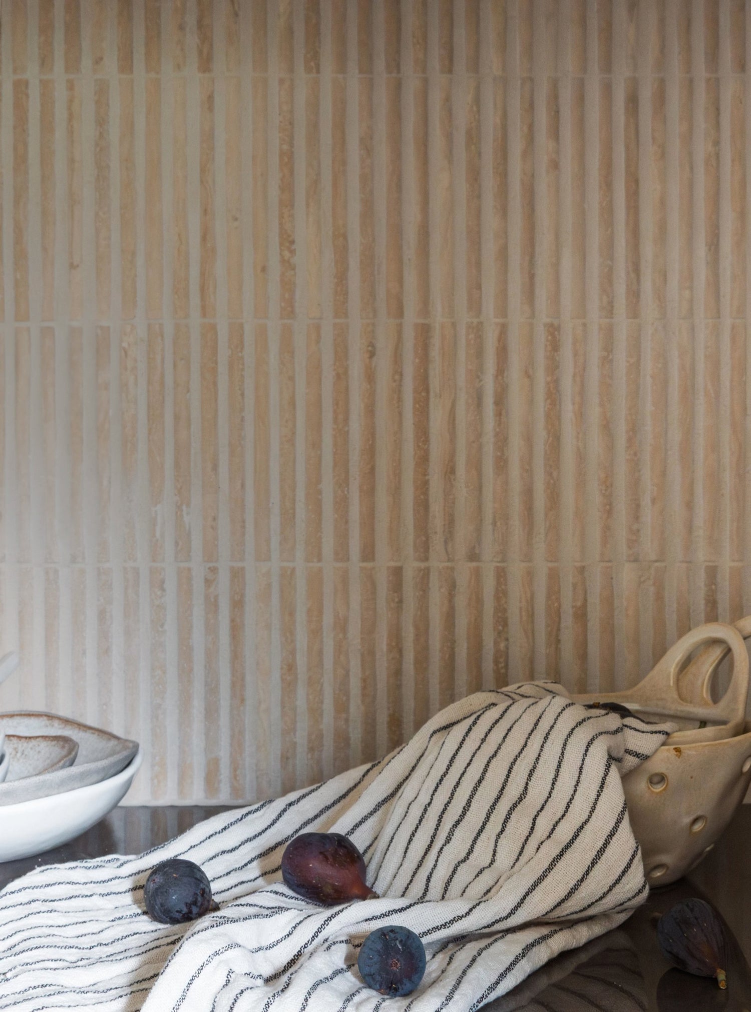 Textured travertine tile wall with a patterned fabric and fruit on a table