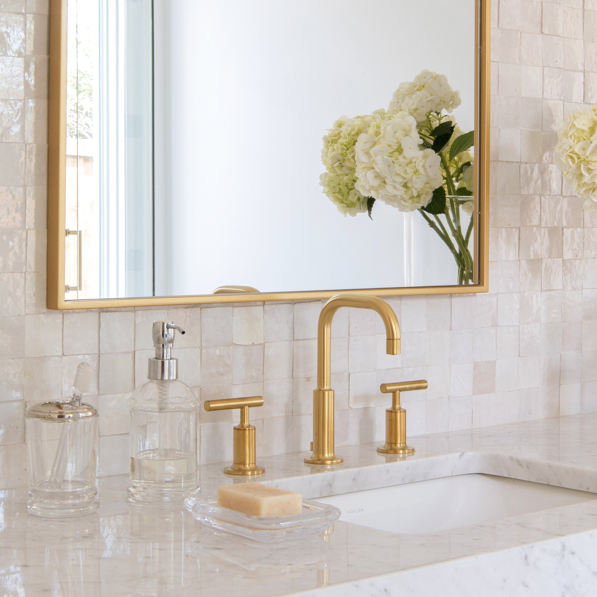 Bathroom sink with gold fixtures, mirror, and zellige backsplash tile.