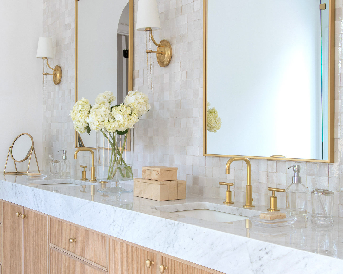 Bathroom vanity with marble countertop, gold fixtures, and zellige backsplash tile.