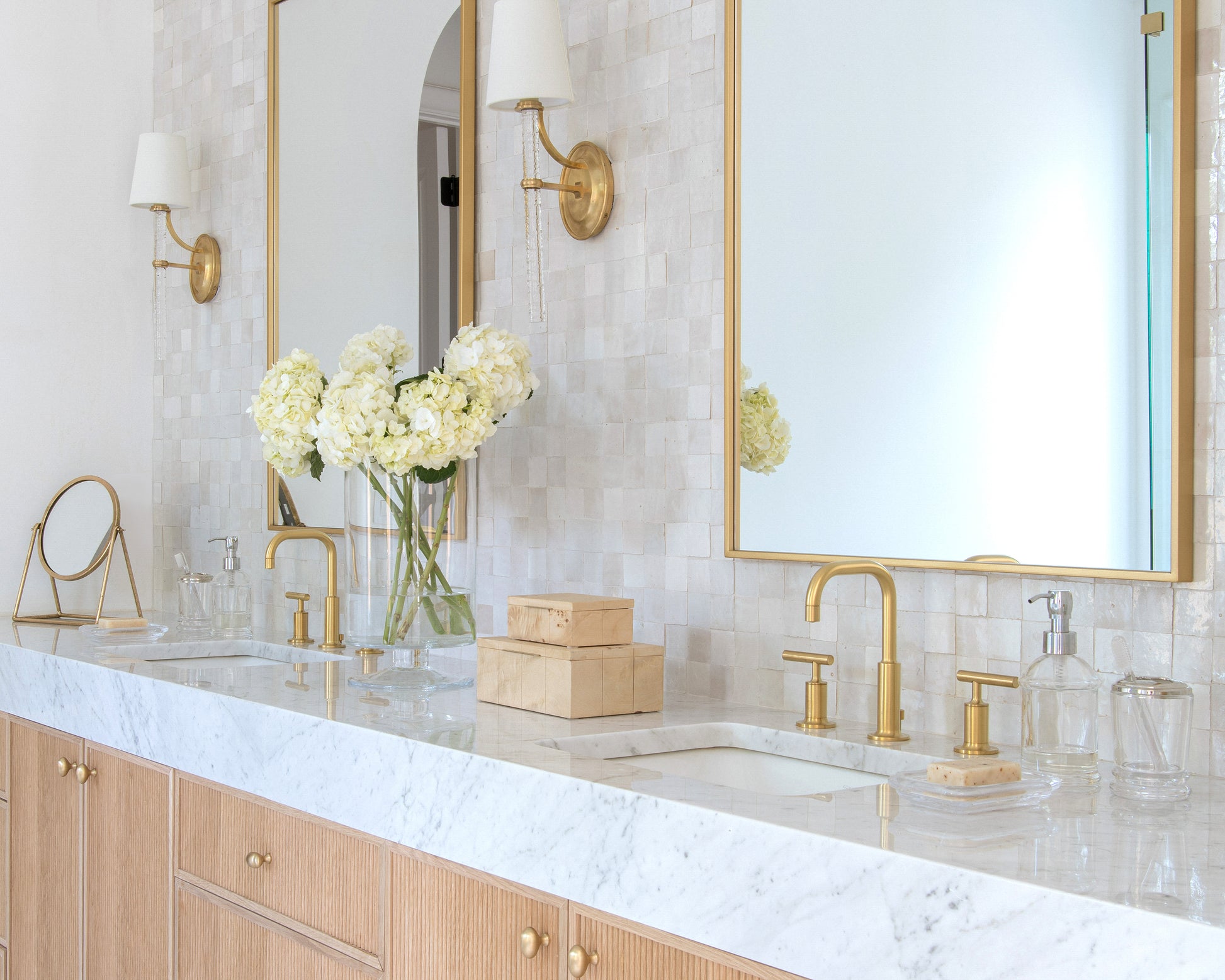 Bathroom vanity with marble countertop, gold fixtures, and zellige backsplash tile.
