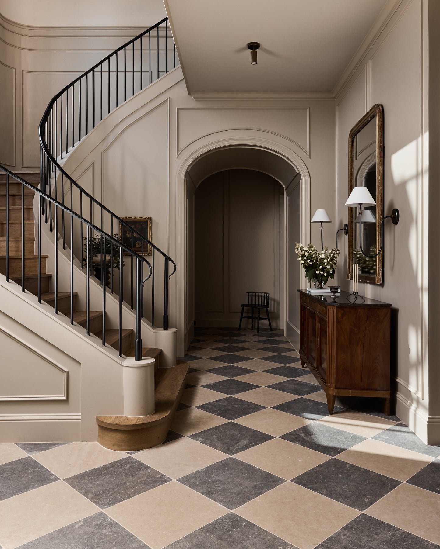 Staircase in a home with checkered limestone floor and wooden furniture.