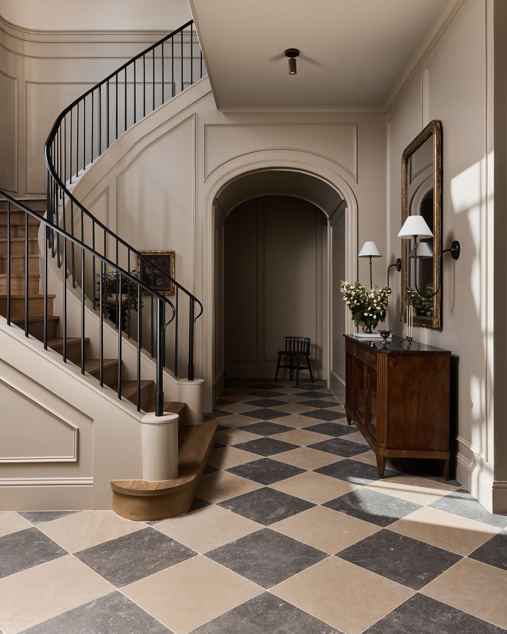 Staircase in a home with checkered limestone floor and wooden furniture.