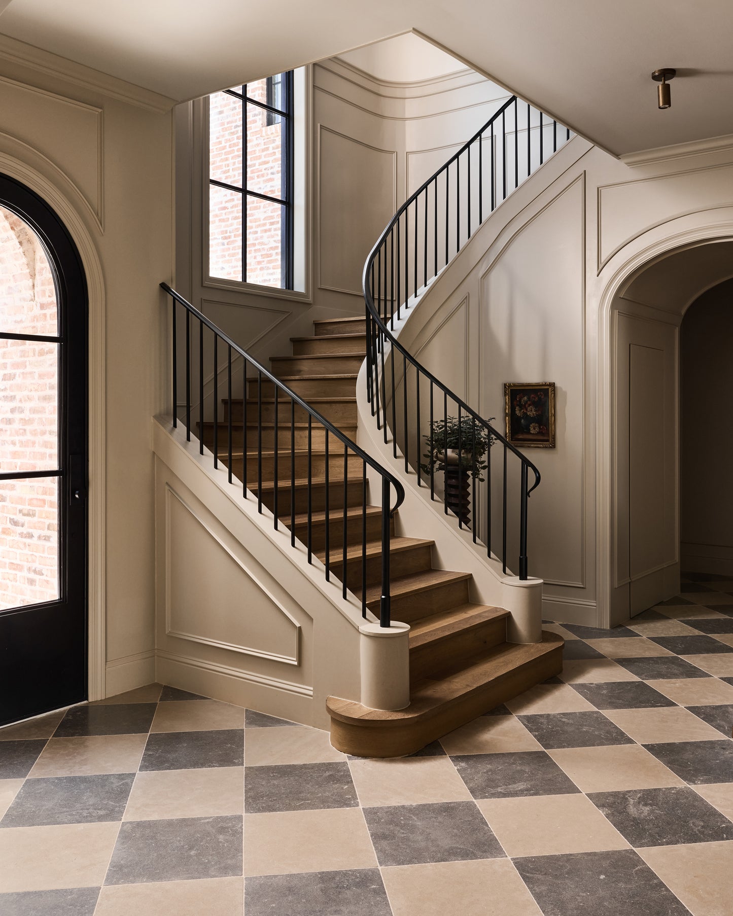 Staircase with black railings in a home interior with checkered limestone floor and arched doorways.