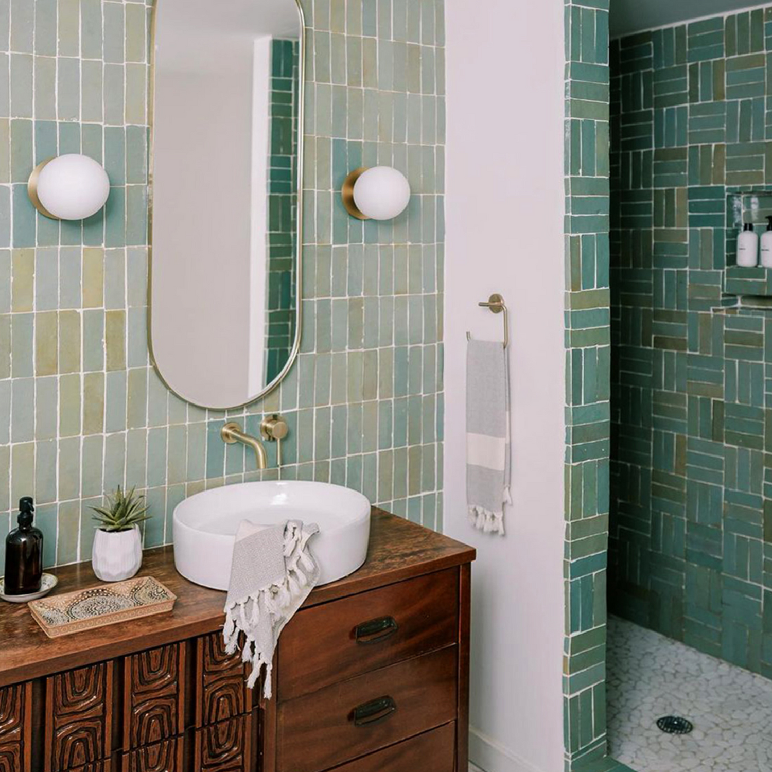 Bathroom with green tiled walls, wooden vanity, and round mirror.