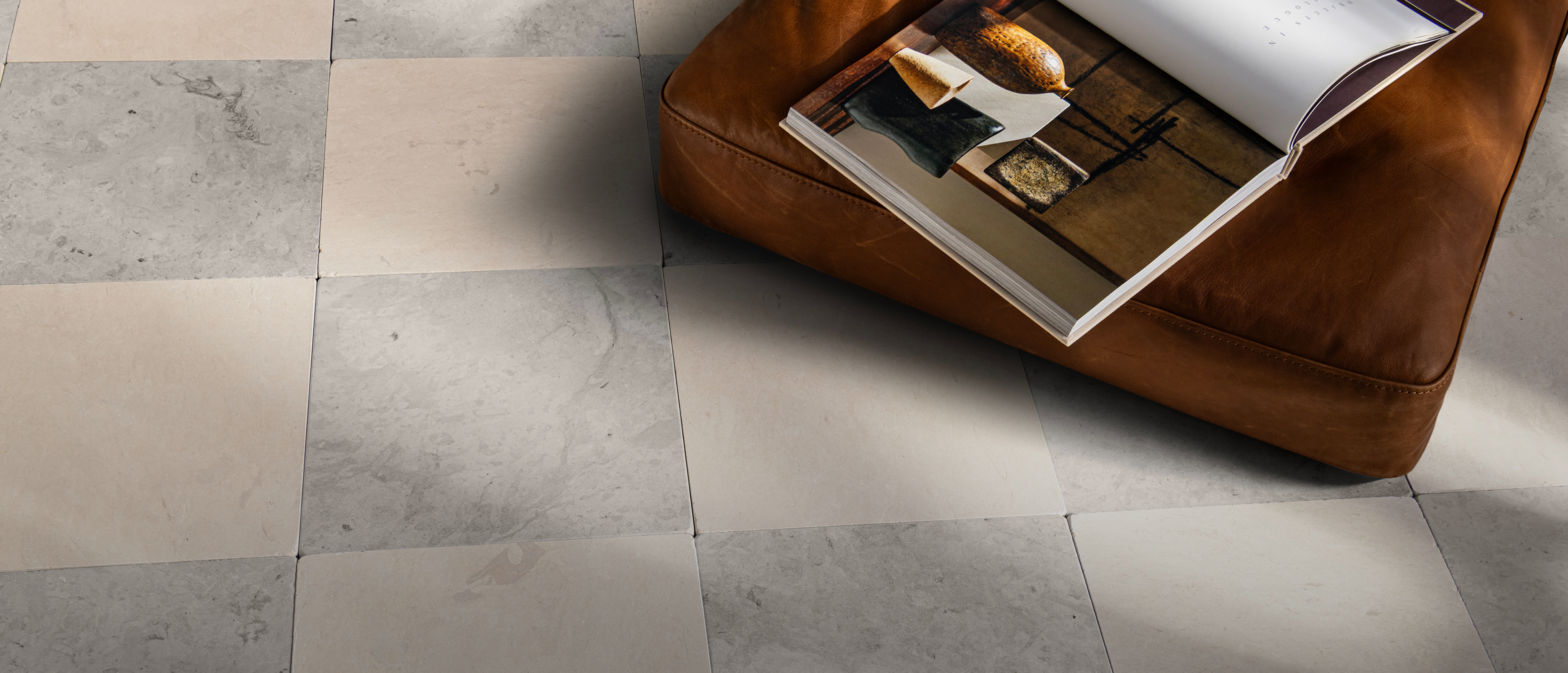 Gray and beige marble-look square floor tiles, with a brown leather ottoman in the upper right holding an open magazine.